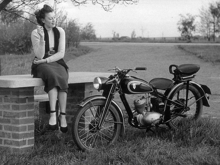 Schwarz-weiß-Aufnahme von einer Frau mit Zigarette neben einer DKW RT 125 W